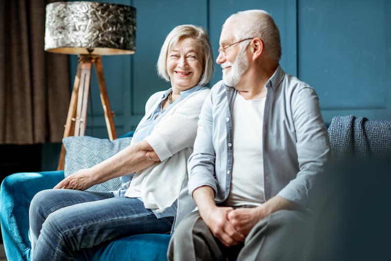 Happy senior couple sitting on couch for their reverse mortgage counseling.